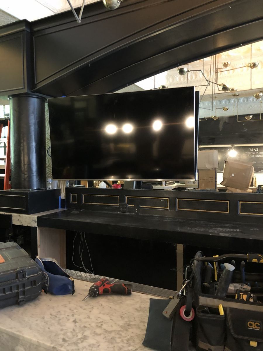 Flat-screen TV mounted above a commercial bar with the lights reflecting on its screen
