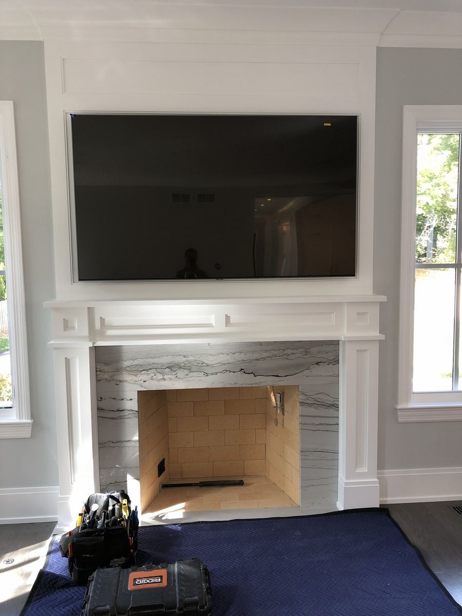 TV mounted above a white fireplace mantel with tools still on the hearth during the install