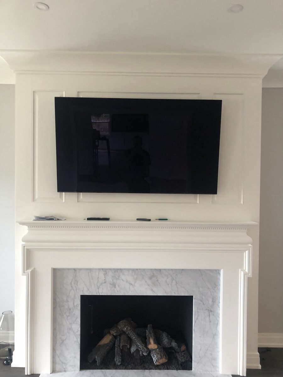 Flat-screen TV mounted over a white fireplace mantel with marble surround