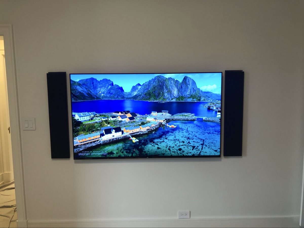 TV mounted on a wall, flanked by wall-mounted speakers